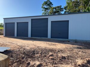 Wide white storage shed with four dark grey doors