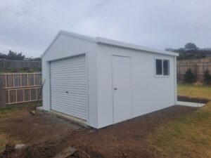Small white shed with roller door and hinge door.