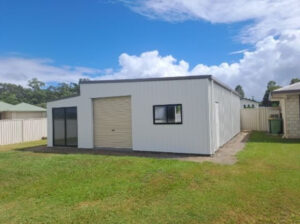 Large white backyard shed with one window, one roller door, and sliding glass door