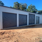 Wide grey shed with 4 roller doors, one higher than the other three.