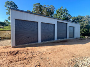 Wide grey shed with 4 roller doors, one higher than the other three.