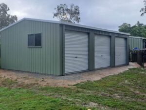 Wide, green utility shed with 3 white roller doors.
