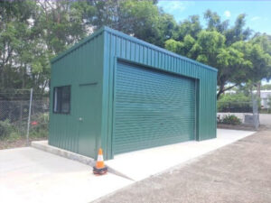 Peacock green shed with window, hinge door, and large sliding roller door. Built on cement slab.